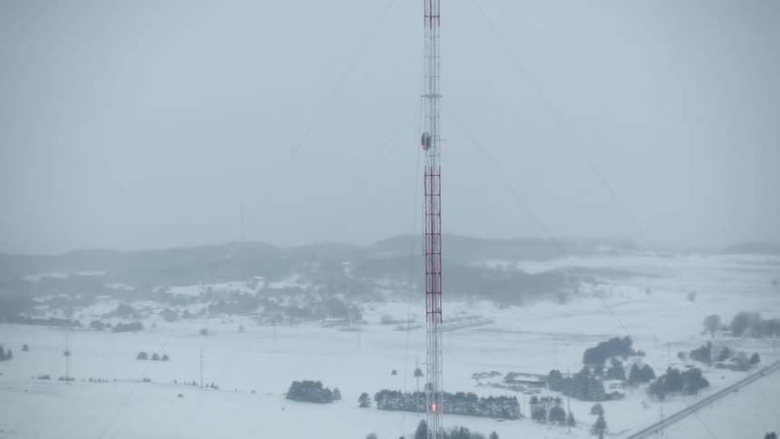 Aerial view orbiting a radio transmission antenna towering over the snowy landscape at winter