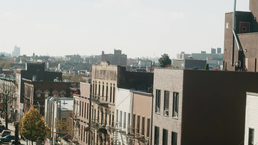 People walk down the street passing by apartment buildings and vehicles on sunny day in city