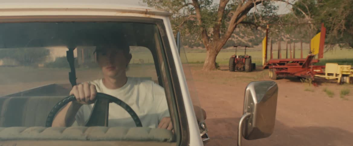 Young man wearing a baseball cap drives a truck on a countryside road at morning