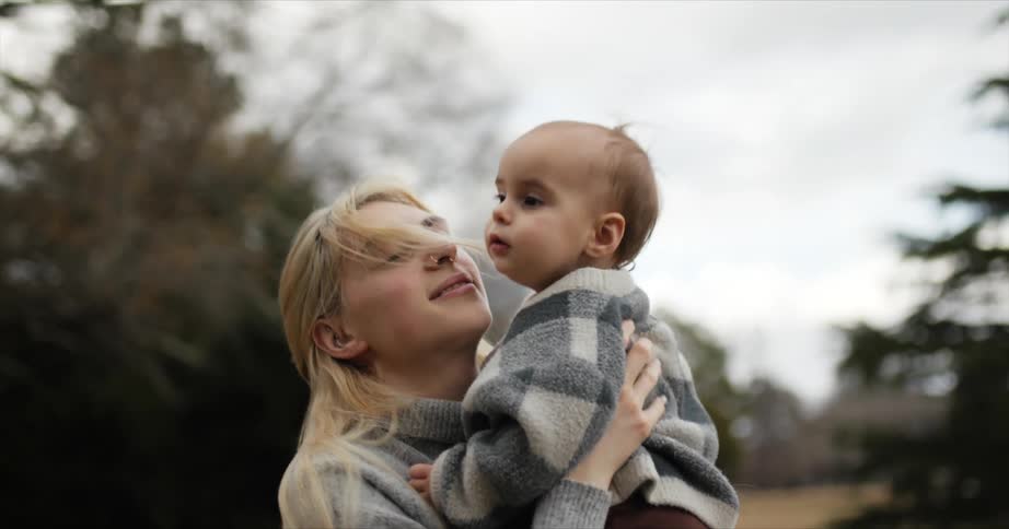 A mom bends and picks up her daughter holding her in the park