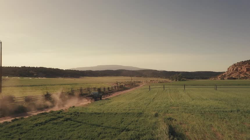 A pickup truck travels on a country farm road with mountains on the horizon