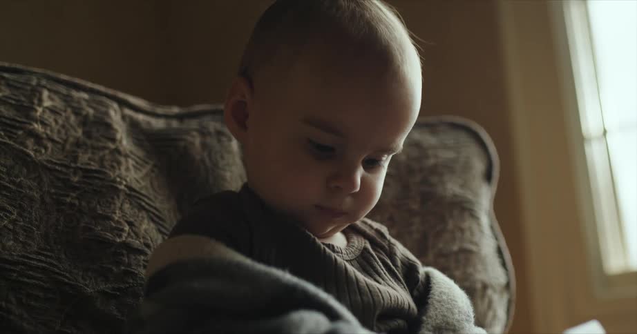 Baby sitting at an armchair while playing with a toy