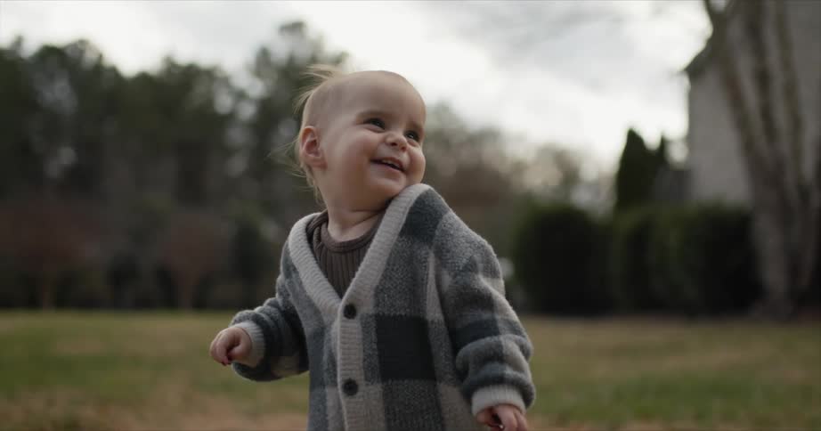 Toddler stands in field near building smiling