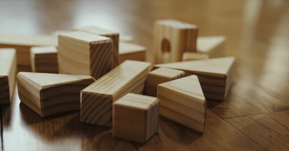 Toddler wearing a sweater picks up wooden block sitting on a pile of blocks on the floor