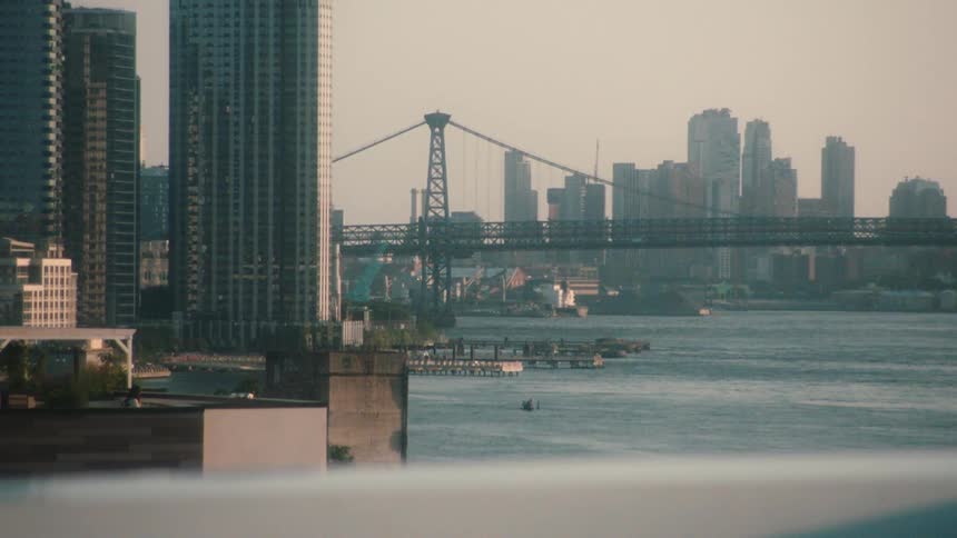 Suspension bridge over river with distant high rise buildings in the city