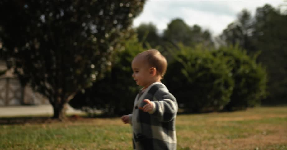 A little girl wearing a big cardigan smiles as she runs across the grass