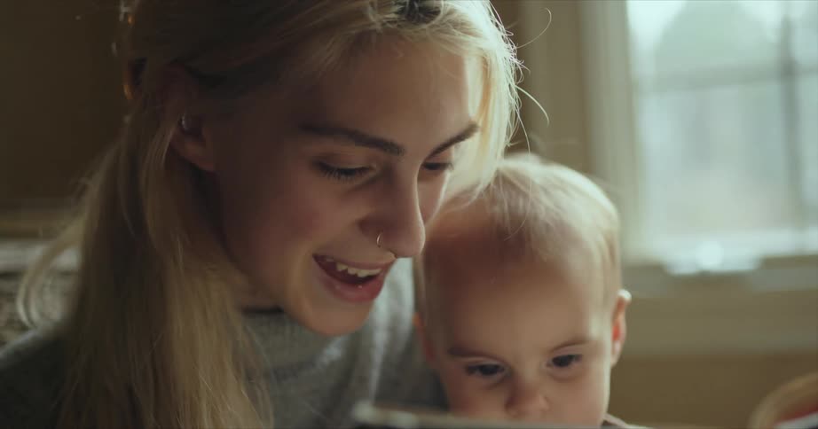 Young mother reading to her baby indoors near a window