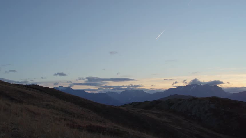 Light snow on a mountain top as a jet plane flies above the clouds in the distance