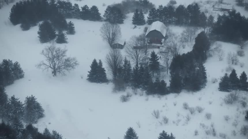 Aerial of house in the woods surrounded by snow during a blizzard
