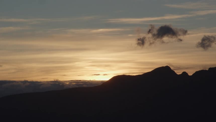 Silhouette of mountains under a cloudy sky as the sun is setting on the horizon