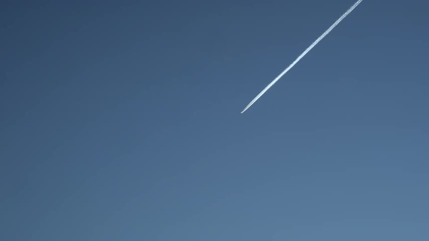A jet plane flying in a clear blue sky leaves behind a contrail