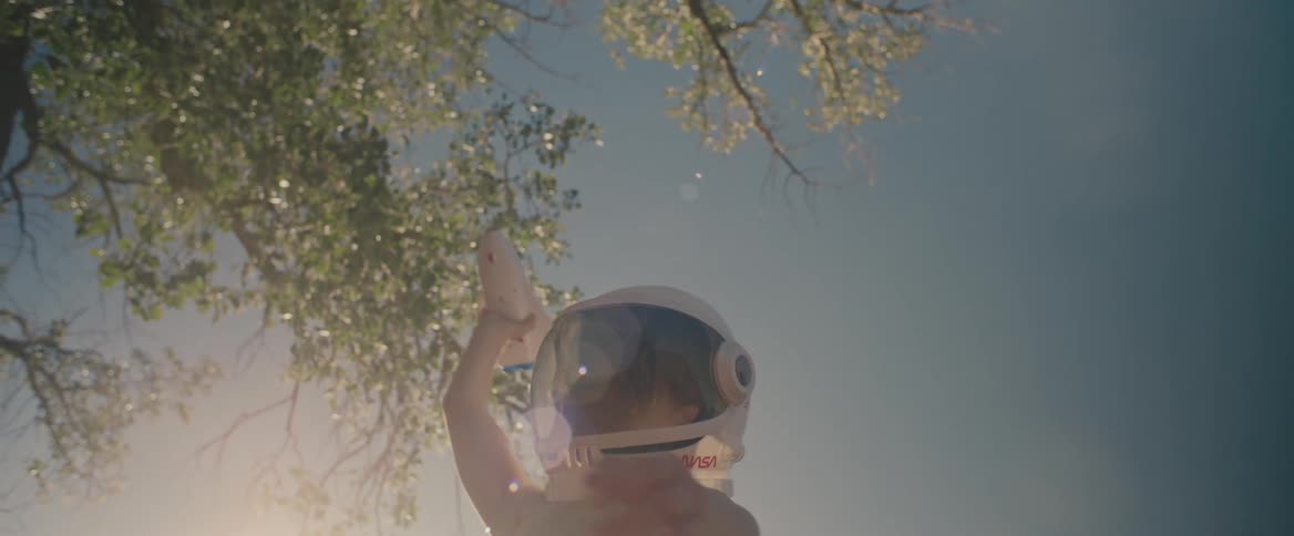 Young shirtless boy wearing a toy astronaut helmet playing with a space shuttle toy outdoors