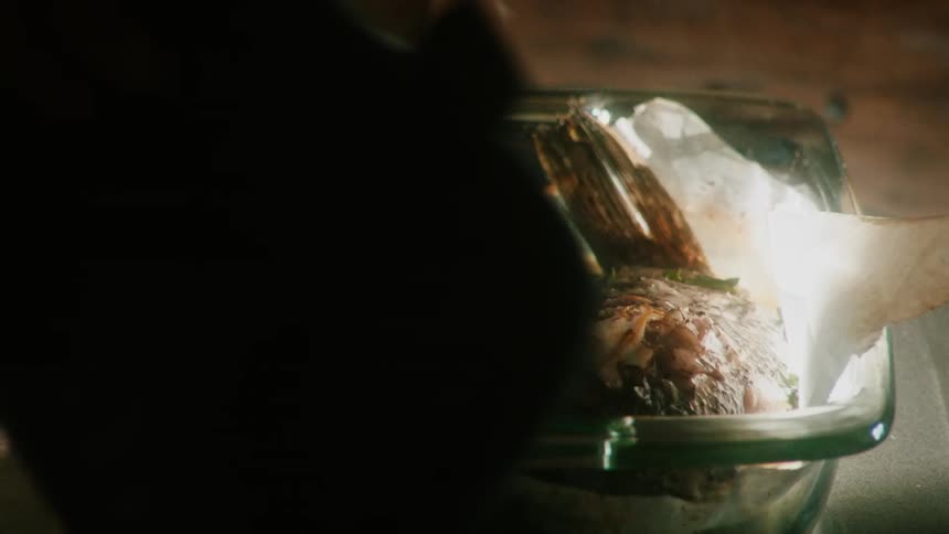 A person picks up a dish with steaming food in it