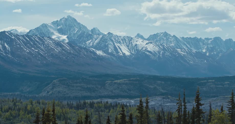 Snow covered mountain range with peaks high in a cloudy sky and a forest of trees below