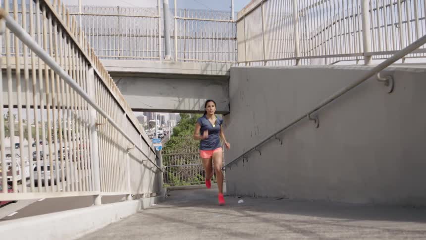 A female runner runs up a ramp to an overpass bridge