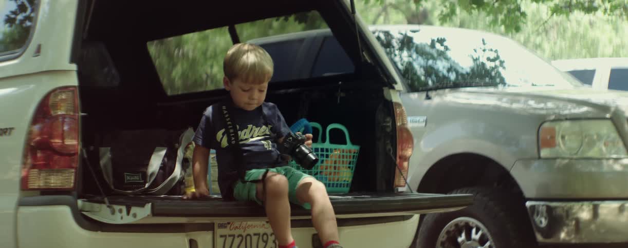 Little boy sitting on a tailgate looking at a camera