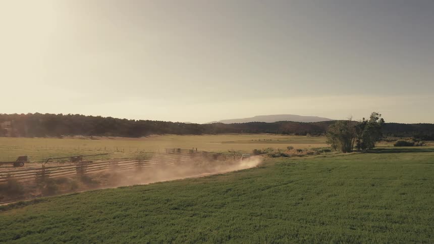 A pickup truck travels on a rural dirt road with mountains on the horizon