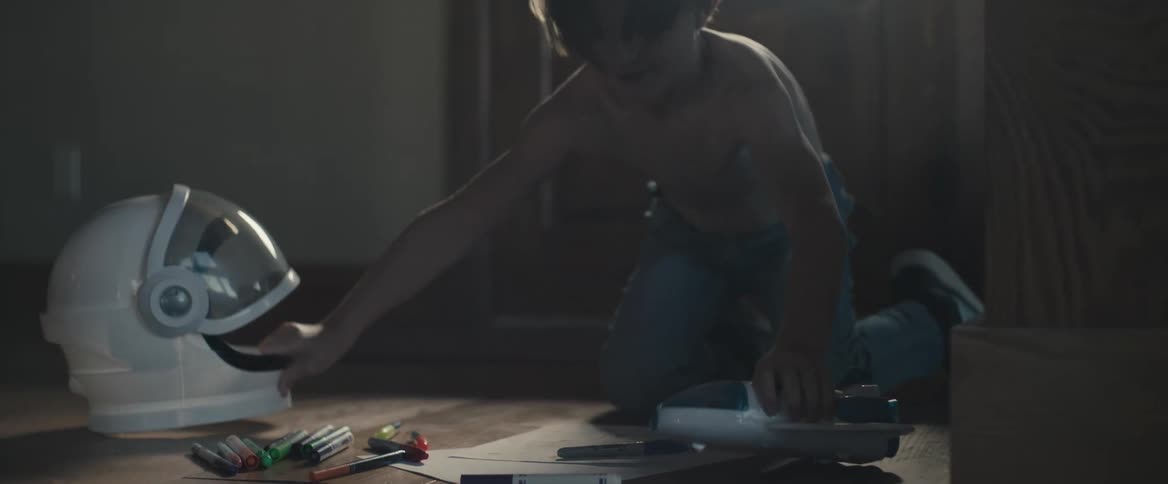 A boy lying in the floor drawing with coloring pens and then picking up his astronault helmet and spaceship toys and starts running