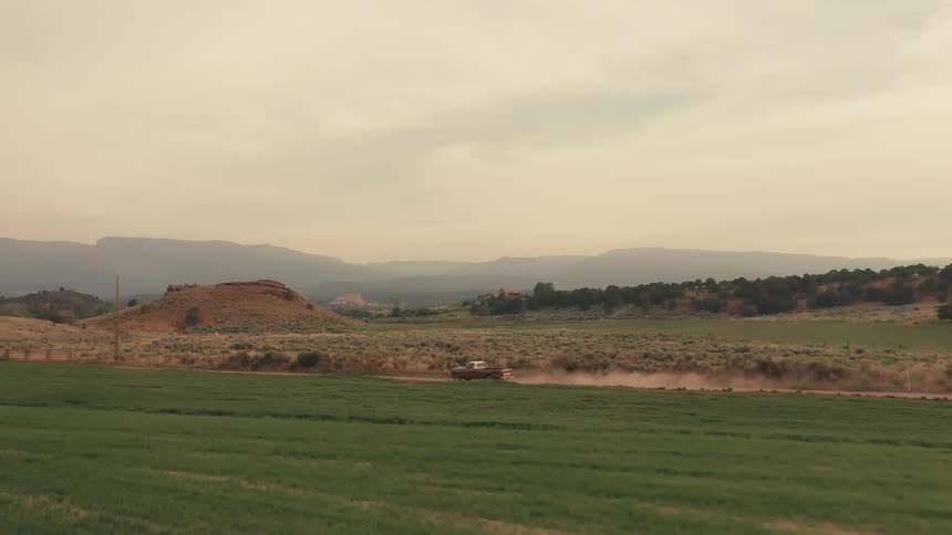 A pickup truck travels on a rural dirt road with mountains in the distance