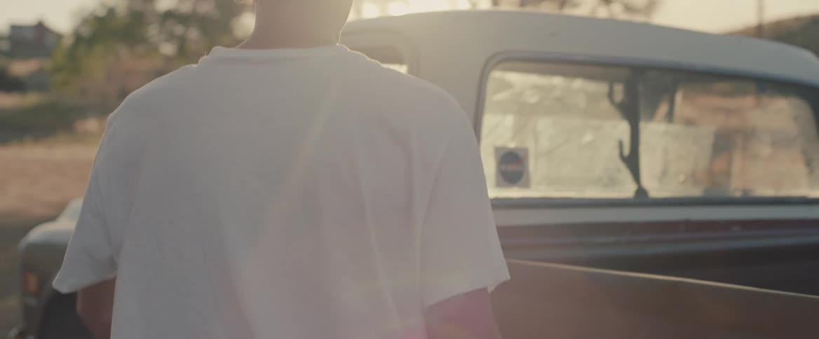 Young man wearing baseball cap walks from his house to a car in the countryside at morning