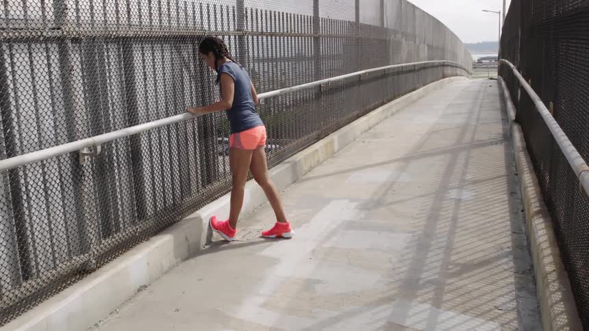 A woman on an overpass stretches her calves