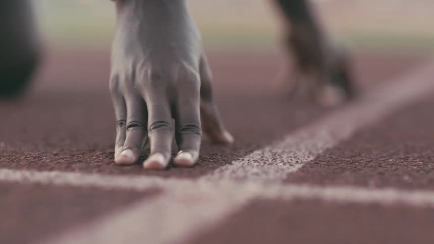 A track athlete sets her hands at the start line