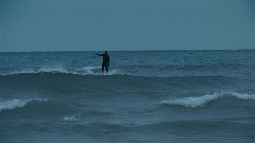 A surfer is surfing on turbulent ocean waves on a cloudy day