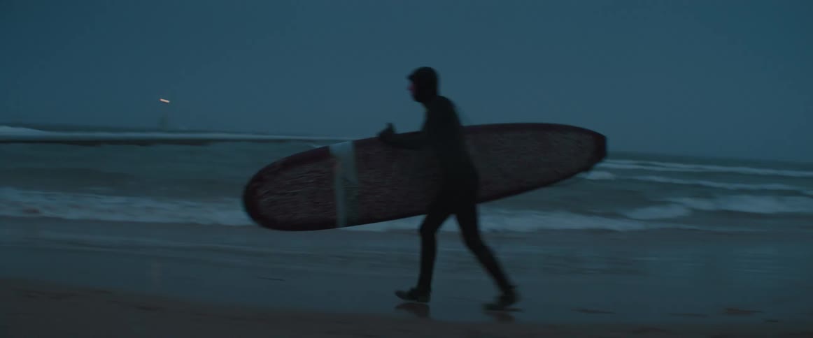 A person running down a beach carrying a surfboard in the winter