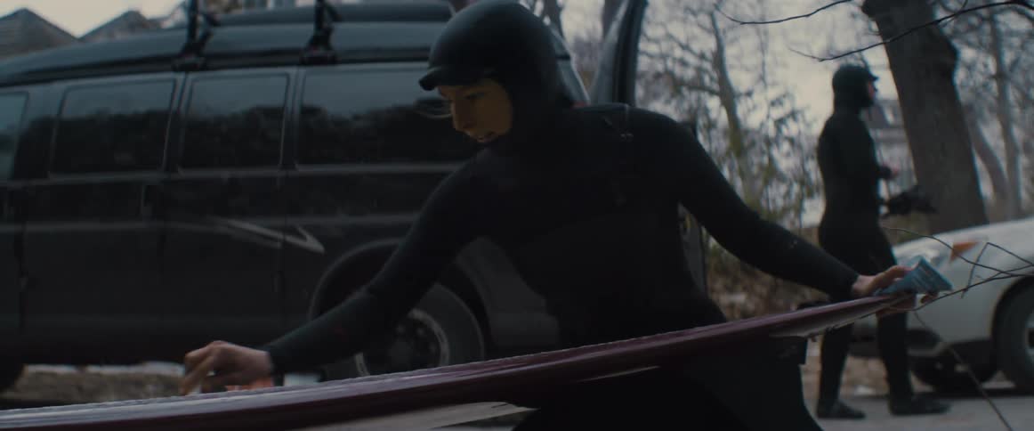 A woman in a wetsuit waxing a surfboard