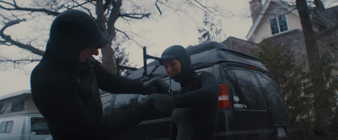Two people are putting on gear outdoors next to their car