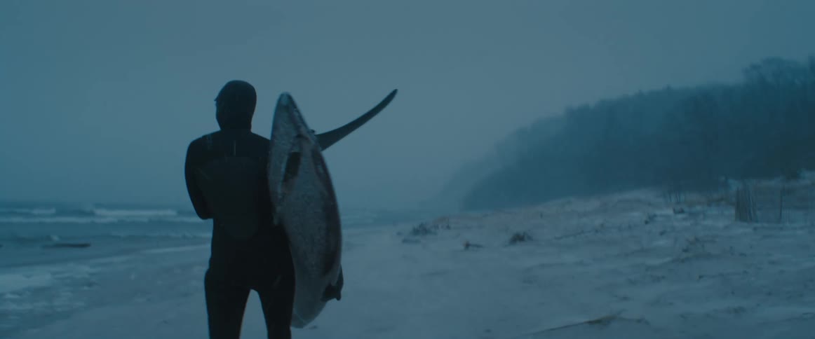 A person walking on the beach in the winter with a surfboard