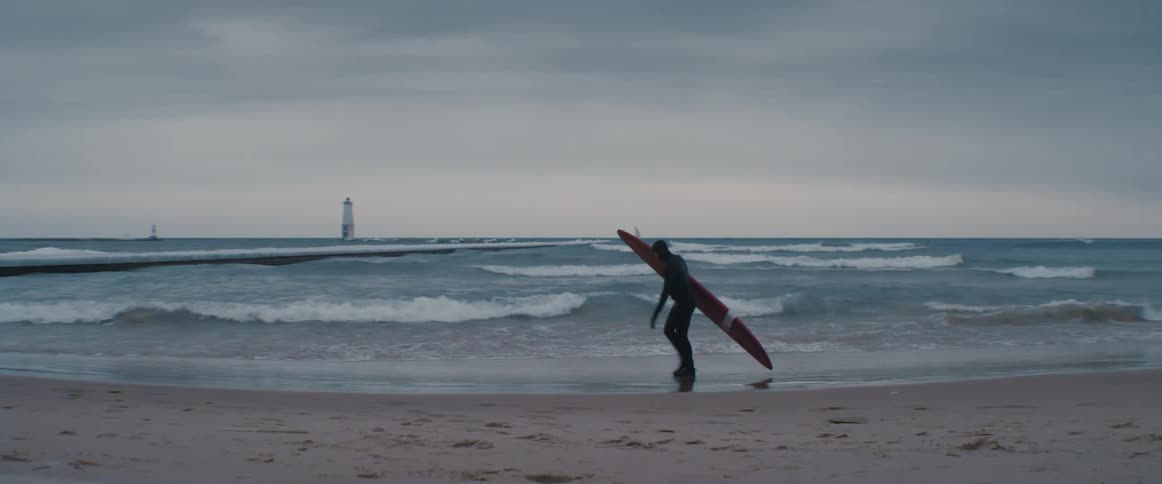 A person is walking on the coast of a beach with a surfboard