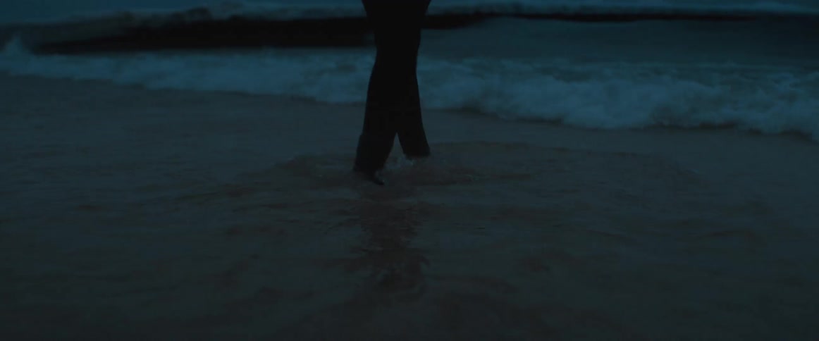 The legs of a person wearing a wet suit wading and walking in the ocean