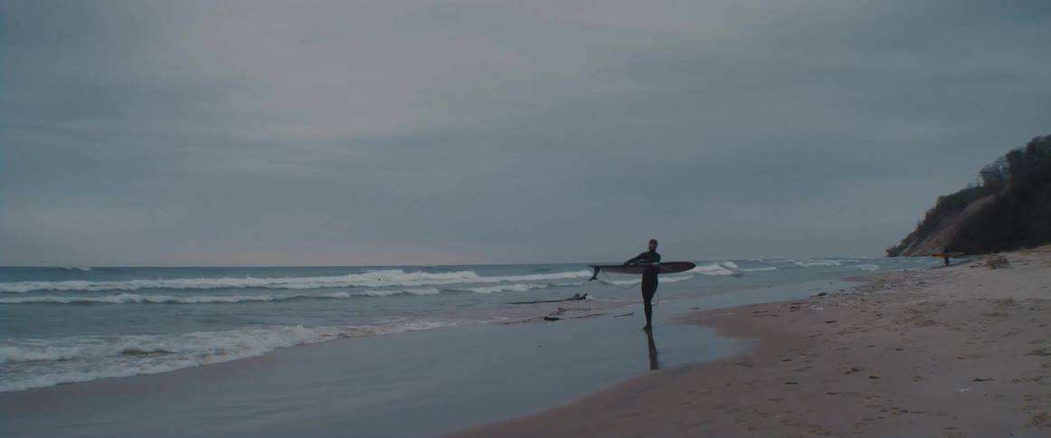 A person carrying a surfboard on the beach in the winter