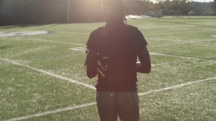 Person carrying a folding chair across a field used for sports at sunset