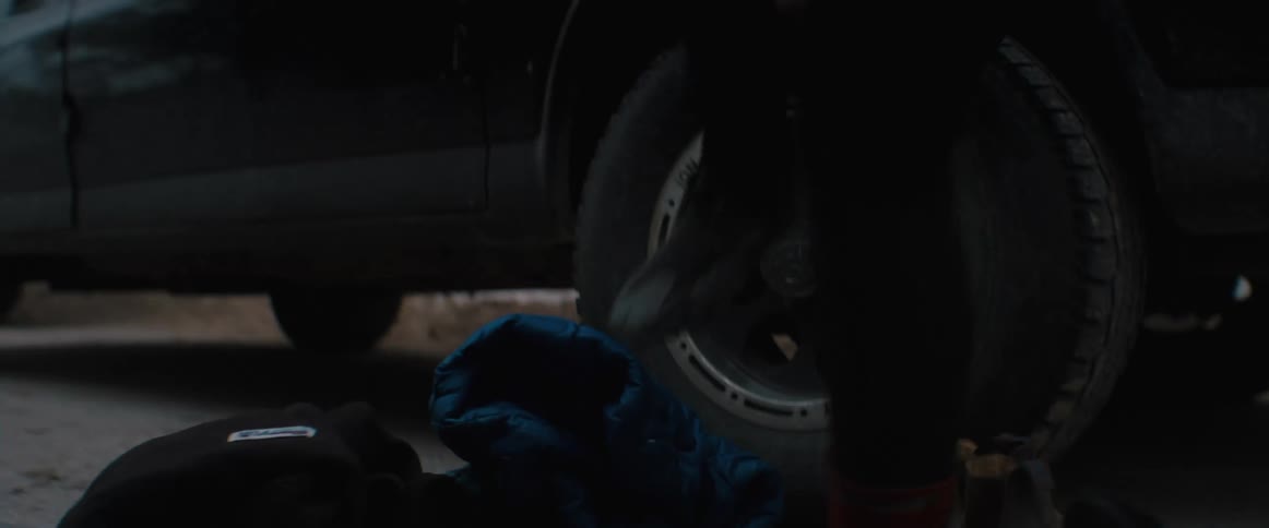 A person is putting on shoes outside next to a car