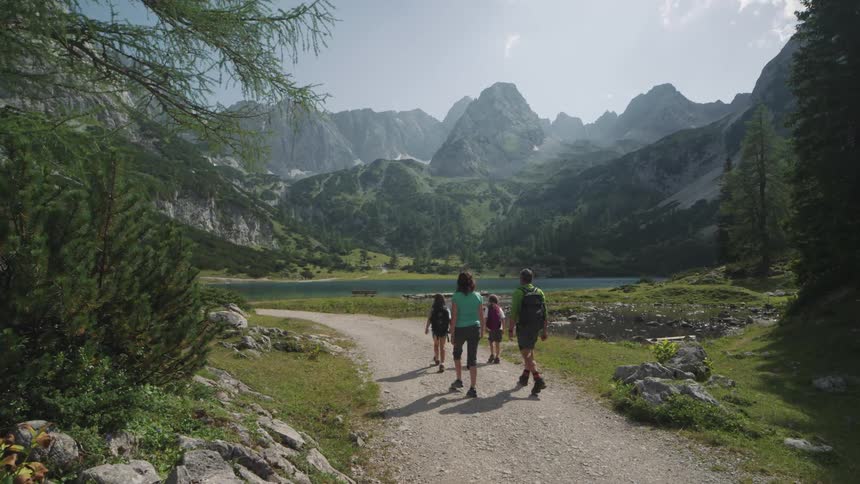Family of four walking on a road towards a lake between the mountains at daytime