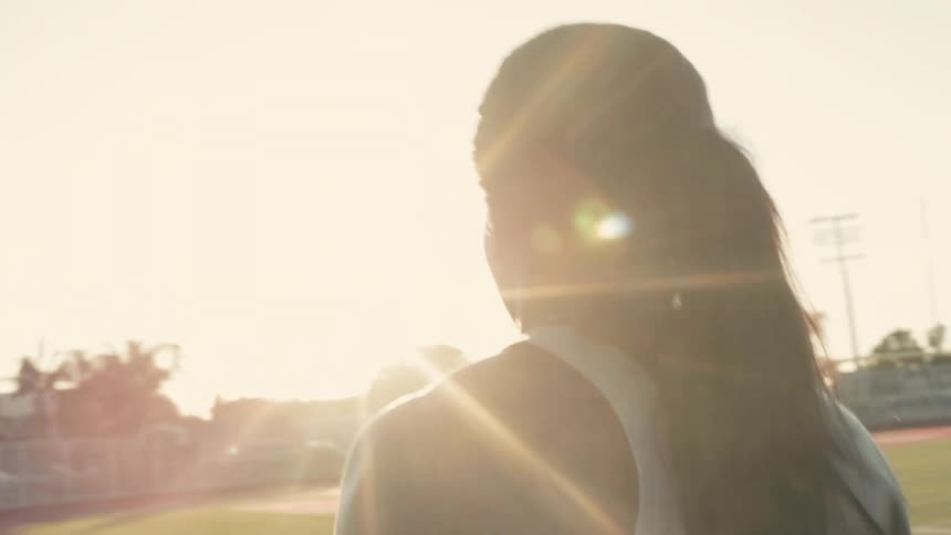 An athlete walking on a track field is highlighted by the sun