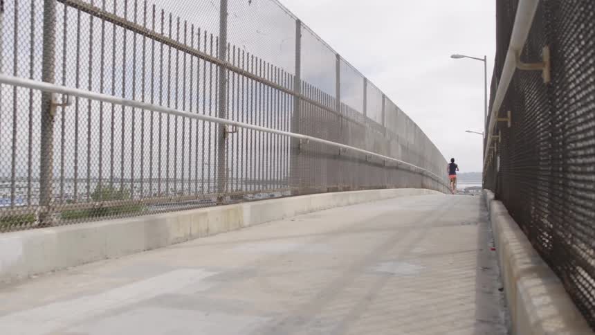A woman runs over a concrete overpass on a cloudy day