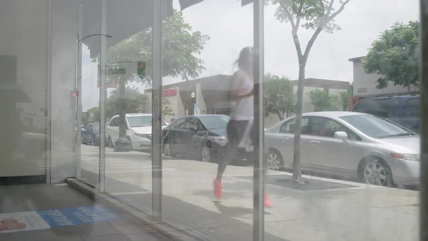 A woman jogs by storefront windows on a sunny day