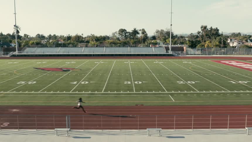A woman running a racetrack that surrounds a football field