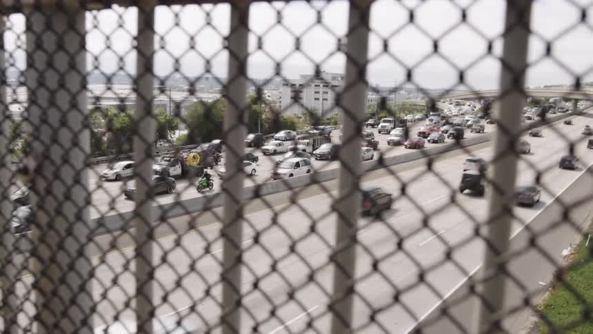 Cars drive below past a fence on an overpass