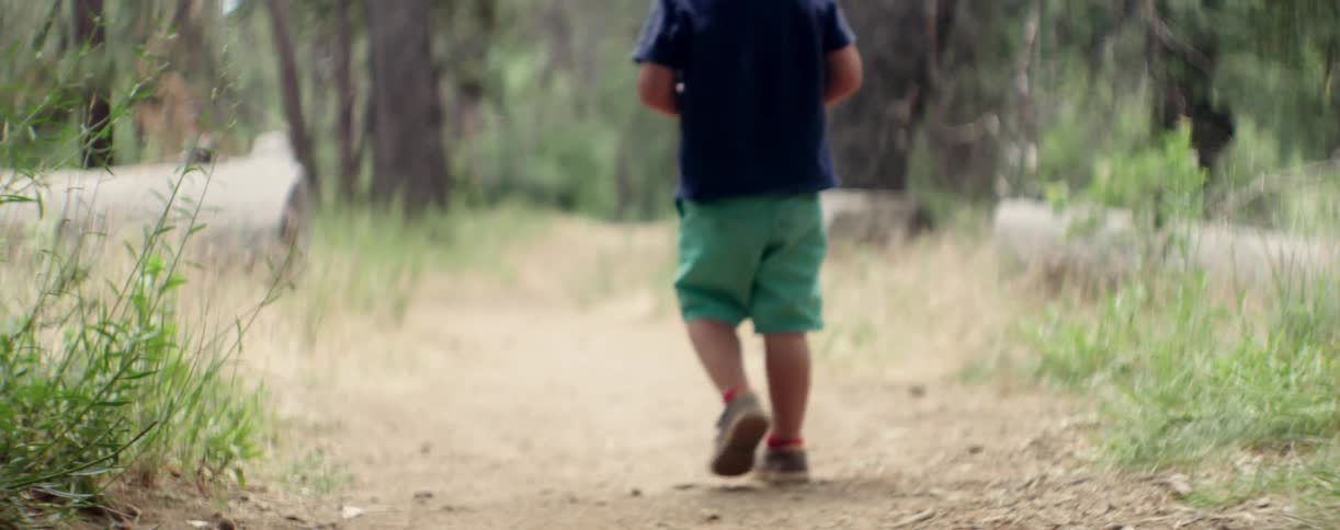 A child is walking down a dirt trail before turning around with a remote in their hands