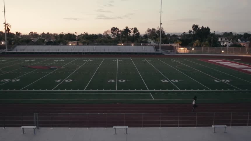 Person running on a track next to a football field
