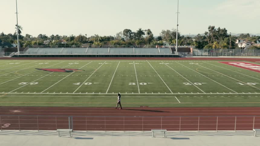 A runner walking a racetrack that circles a football field