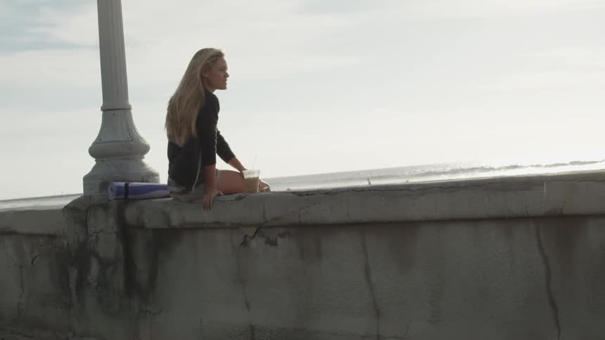 Woman sitting on a concrete wall by the ocean
