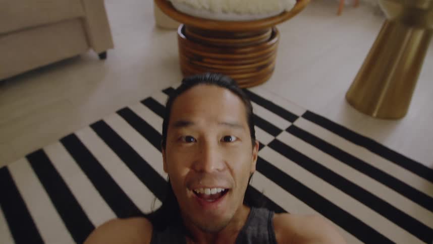 A man is filming himself doing stomach crunches on the floor in a living room during the day