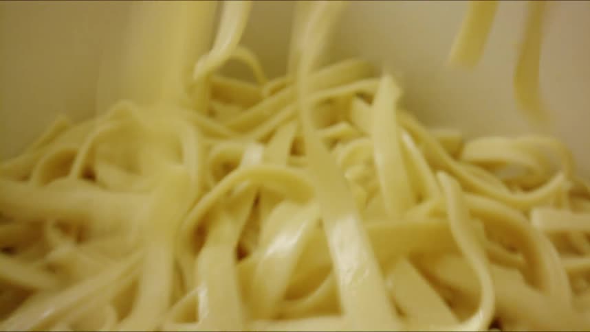 Wet pasta noodles are being sprinkled into a dish while indoors