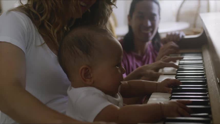 A baby plays the piano with his mother