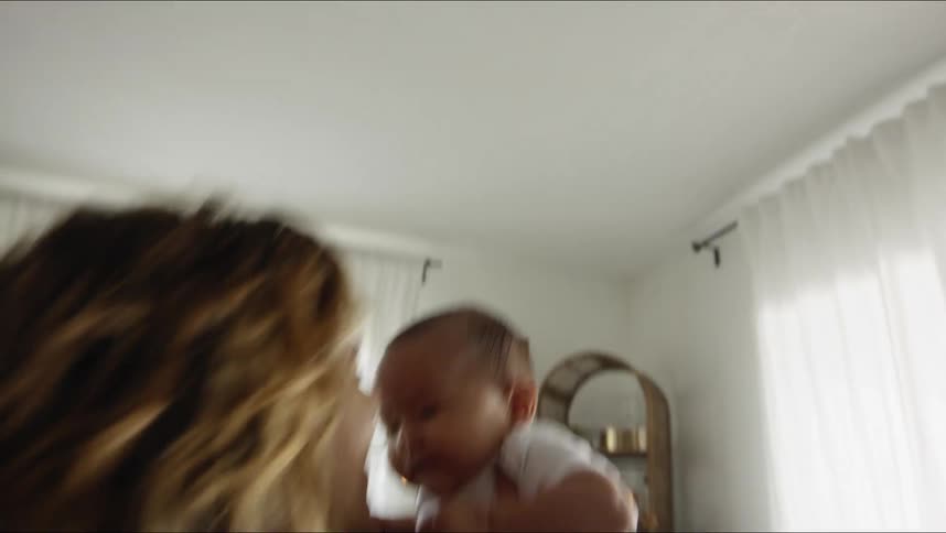 A woman holds her baby and plays with them in the air